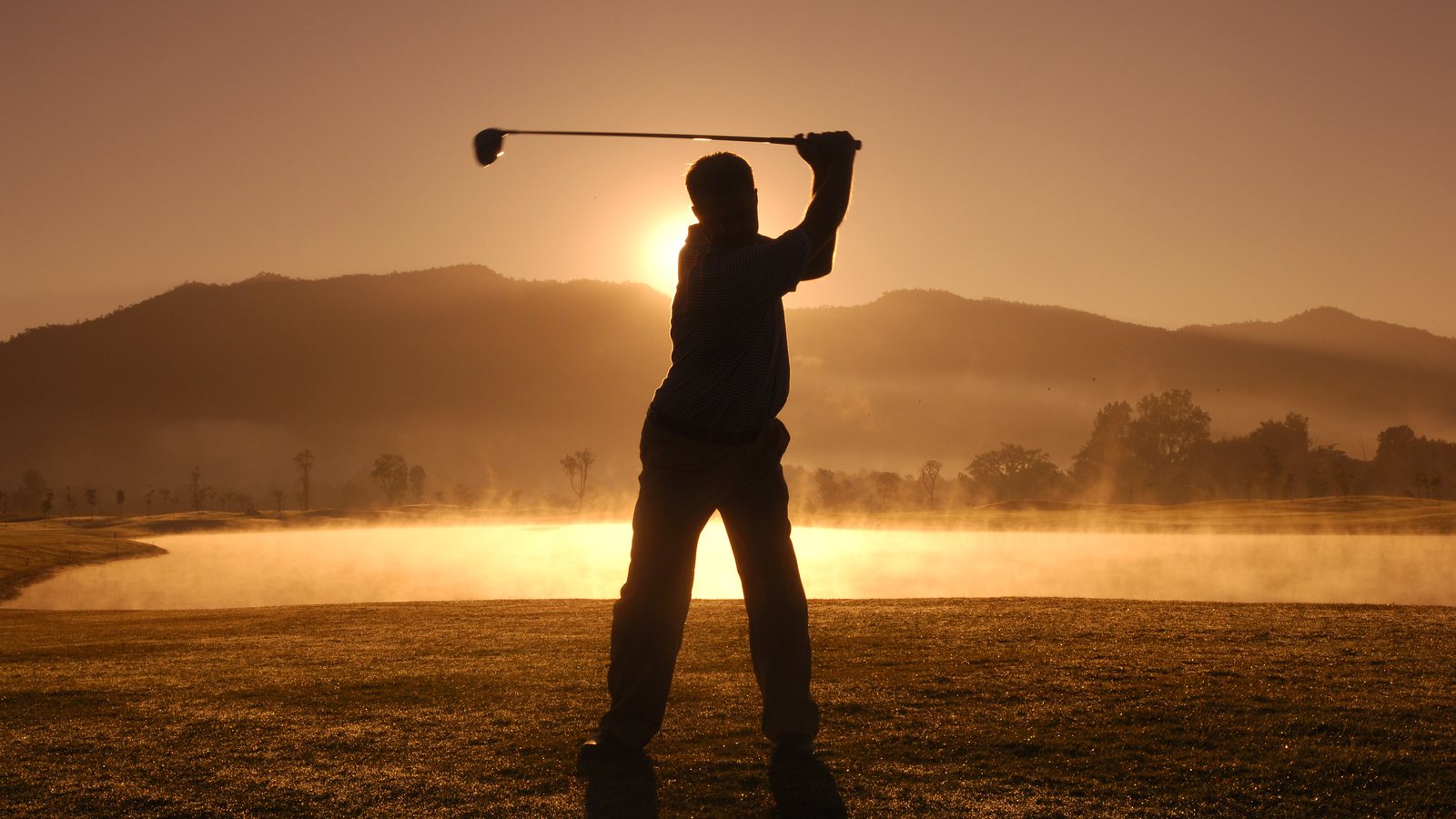 Golfer swinging at sunset