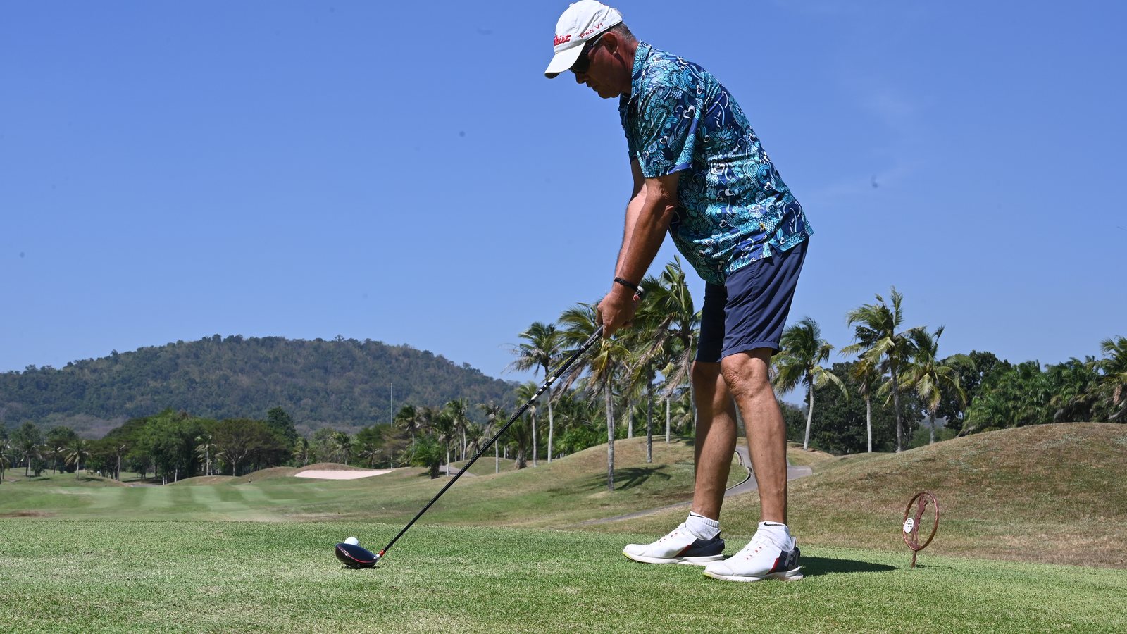 Golfer lining up a tee shot in tropical sunlight